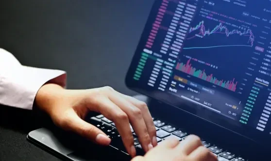 Close-up of a professional typing on a keyboard while analyzing real-time financial charts and data graphs on a screen