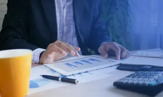 Professional analyzing financial bar charts on a tablet alongside printed reports and a calculator
