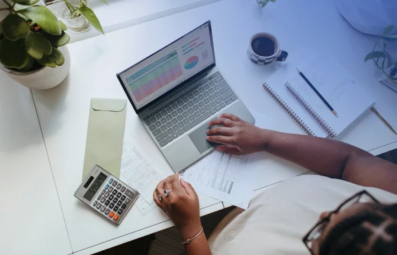 Overhead view of a professional analyzing a digital financial dashboard on a laptop alongside a calculator and printed documents